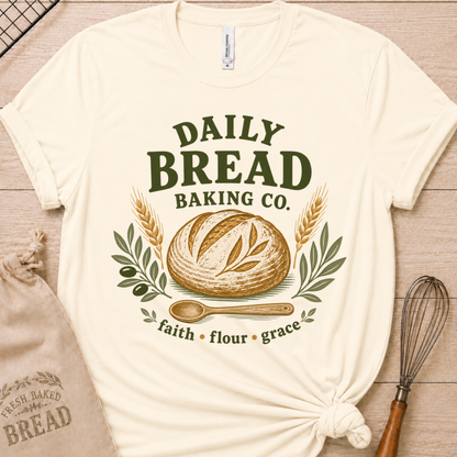 Natural cream women's relaxed fit t-shirt with the Daily Bread Baking Co. design, a retro bakery emblem featuring an artisan bread loaf, wheat stalks, and a wooden spoon above the words faith, flour, grace.