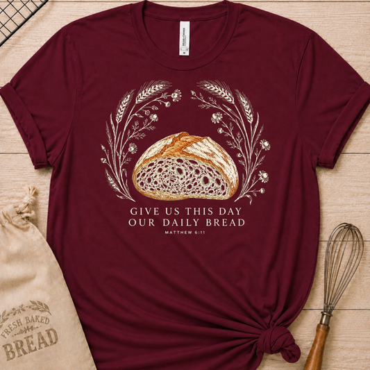Maroon women's relaxed fit t-shirt with the Daily Bread design featuring a rustic loaf of bread wreathed in wheat and flowers, inspired by Matthew 6:11.