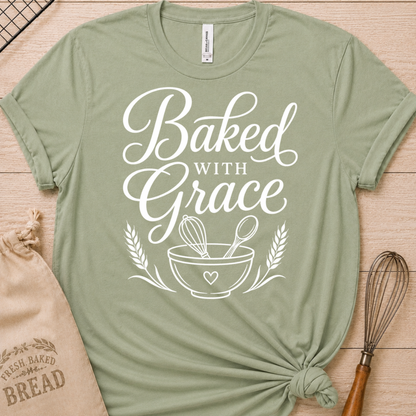 Sage green women's relaxed fit t-shirt with Baked with Grace in white script above a mixing bowl with a whisk and wooden spoon.