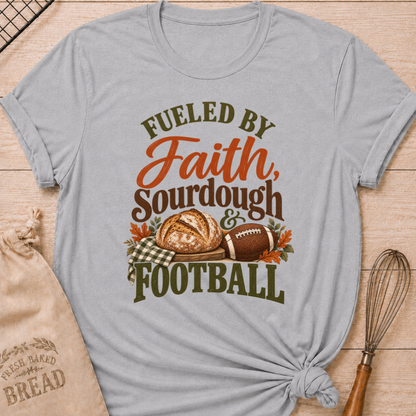 Athletic Heather women's relaxed fit tee with bold vintage Fueled by Faith Sourdough and Football lettering, a rustic sourdough loaf, classic football, gingham accents and autumn leaves