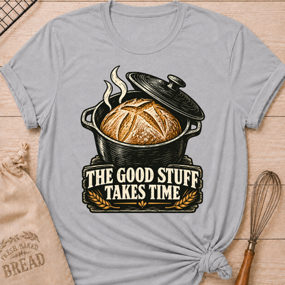 Athletic Heather women's relaxed fit tee with a golden artisan loaf rising from a vintage Dutch oven, steam curling overhead and wheat accents below, with The Good Stuff Takes Time lettering