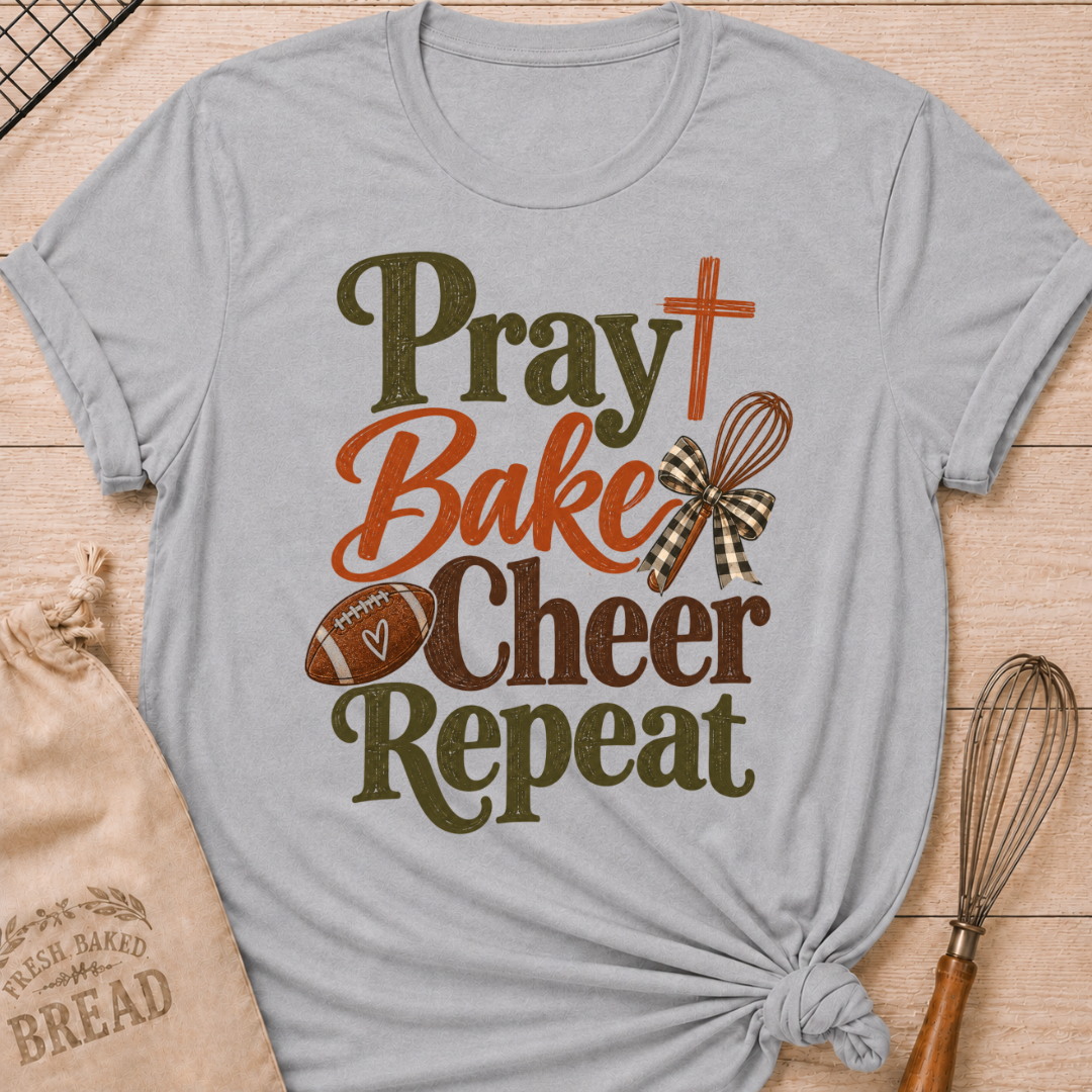 Athletic Heather women's relaxed fit tee with bold vintage Pray Bake Cheer Repeat lettering, a football, whisk, cross and gingham bow in warm autumn tones