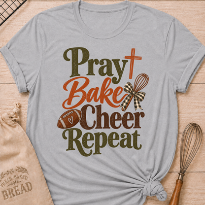 Athletic Heather women's relaxed fit tee with bold vintage Pray Bake Cheer Repeat lettering, a football, whisk, cross and gingham bow in warm autumn tones
