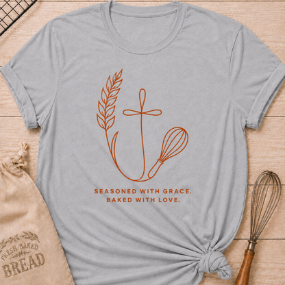 Athletic heather women's relaxed fit t-shirt with the words Seasoned With Grace, Baked With Love in clean line art with wheat, a subtle cross, and a classic whisk.