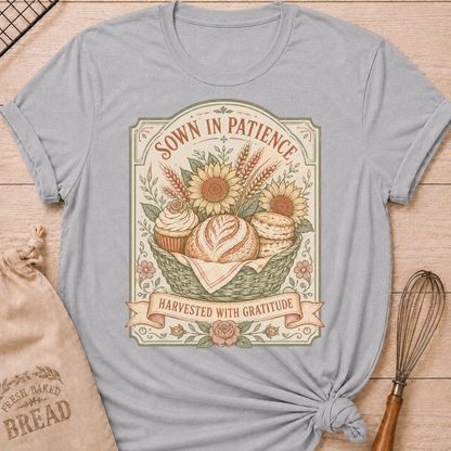 Athletic Heather Sown In Patience, Harvested In Gratitude women's relaxed fit tee with a vintage basket of bread, biscuits, cupcakes, sunflowers, and wheat