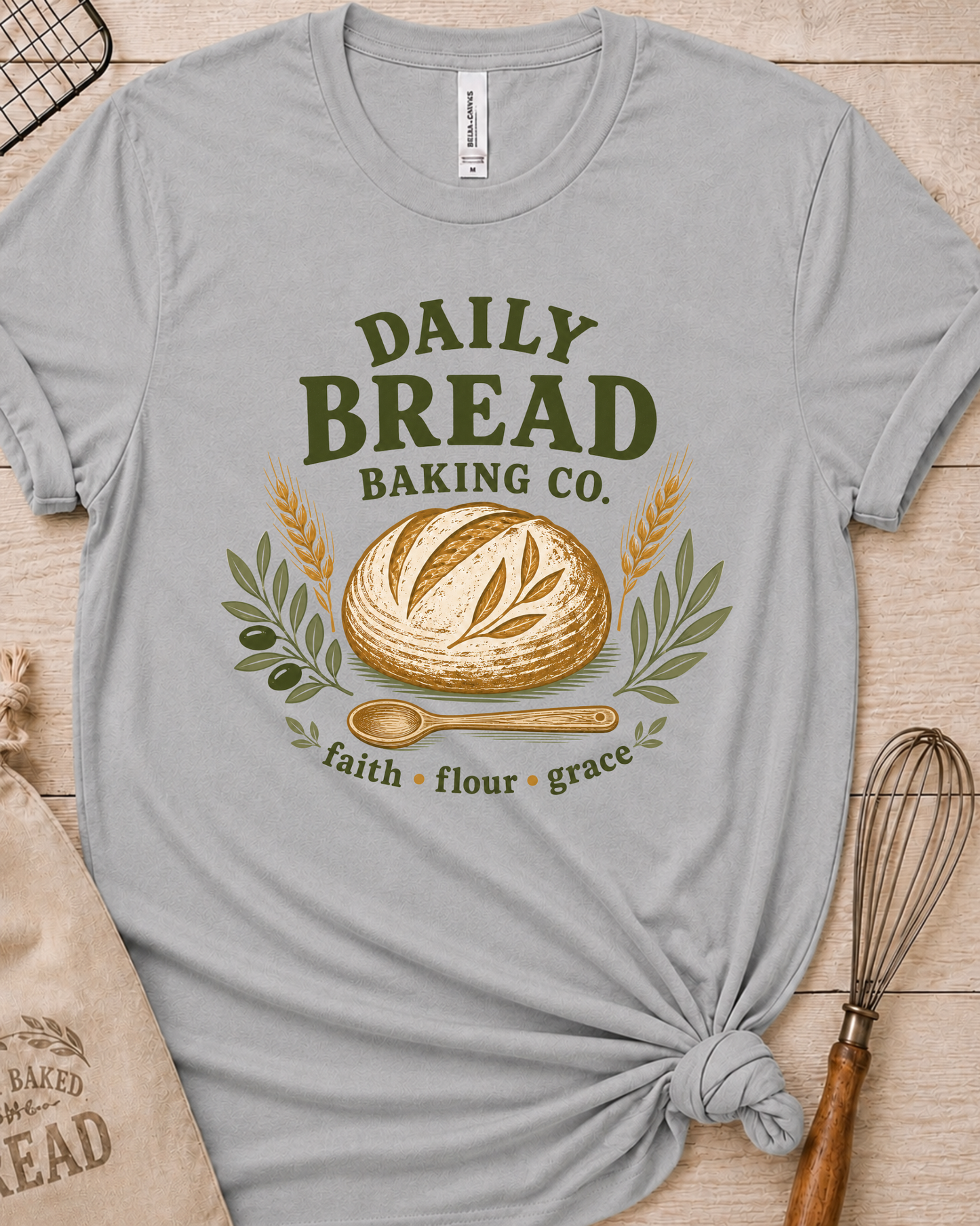 Heather grey women's relaxed fit t-shirt with the Daily Bread Baking Co. design, a retro bakery emblem featuring an artisan bread loaf, wheat stalks, and a wooden spoon above the words faith, flour, grace.