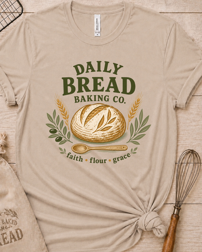 Heather stone women's relaxed fit t-shirt with the Daily Bread Baking Co. design, a retro bakery emblem featuring an artisan bread loaf, wheat stalks, and a wooden spoon above the words faith, flour, grace.