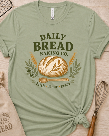 Sage green women's relaxed fit t-shirt with the Daily Bread Baking Co. design, a retro bakery emblem featuring an artisan bread loaf, wheat stalks, and a wooden spoon above the words faith, flour, grace.