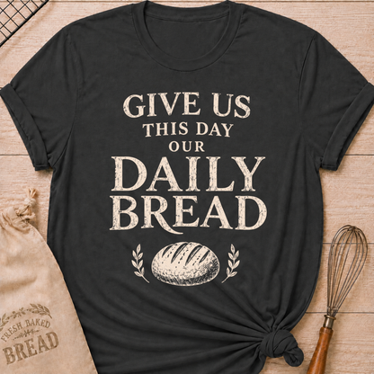 Dark heather grey women's relaxed fit t-shirt with the words Give Us This Day Our Daily Bread in bold vintage lettering above a rustic loaf and leafy accents.