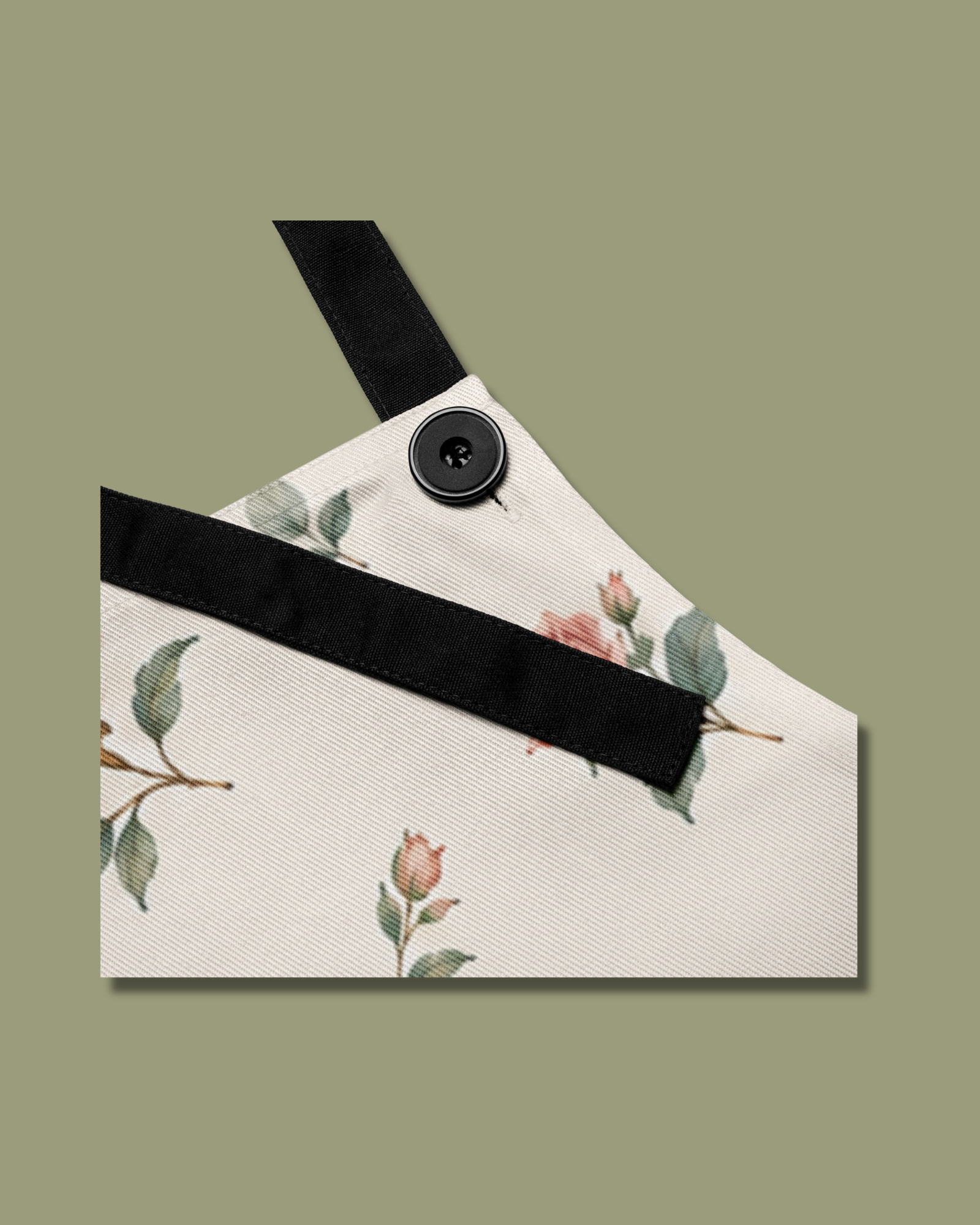 Close-up of the Baked with Grace floral apron showing the black adjustable neck strap and button detail against the cream floral fabric.