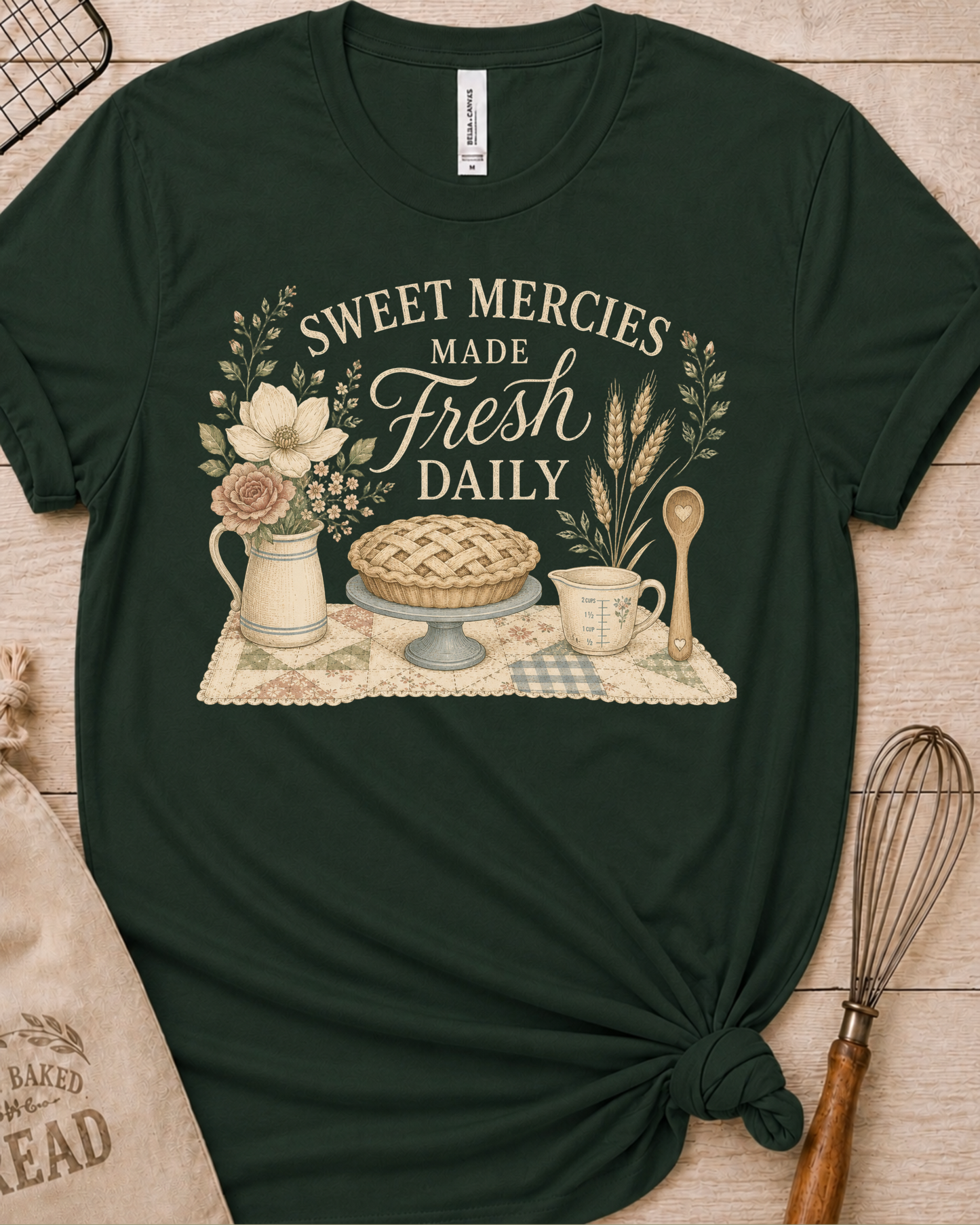 Forest green women's relaxed fit t-shirt reading Sweet Mercies Made Fresh Daily above a lattice-top pie on a cake stand with a flower pitcher, measuring cup, and wooden spoon.