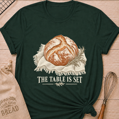 Forest Green women's relaxed fit tee with a rustic artisan loaf resting on softly draped linen with a rosemary sprig and The Table Is Set lettering