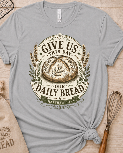 Heather grey women's relaxed fit t-shirt with the Daily Bread emblem printed in cream, a clean badge-style bread illustration inspired by Matthew 6:11.