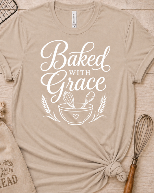 Heather stone women's relaxed fit t-shirt with Baked with Grace in white script above a mixing bowl with a whisk and wooden spoon.
