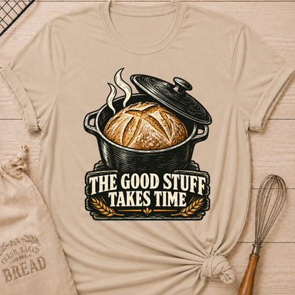 Heather Stone women's relaxed fit tee with a golden artisan loaf rising from a vintage Dutch oven, steam curling overhead and wheat accents below, with The Good Stuff Takes Time lettering