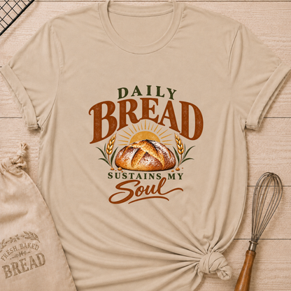 Heather Stone women's relaxed fit tee with Daily Bread Sustains My Soul lettering around a golden artisan loaf beneath a rising sun, framed by wheat in rich earthy tones