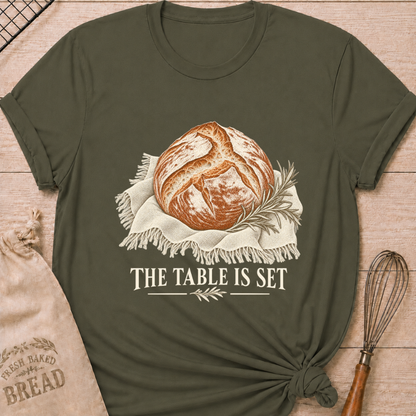 Military Green women's relaxed fit tee with a rustic artisan loaf resting on softly draped linen with a rosemary sprig and The Table Is Set lettering
