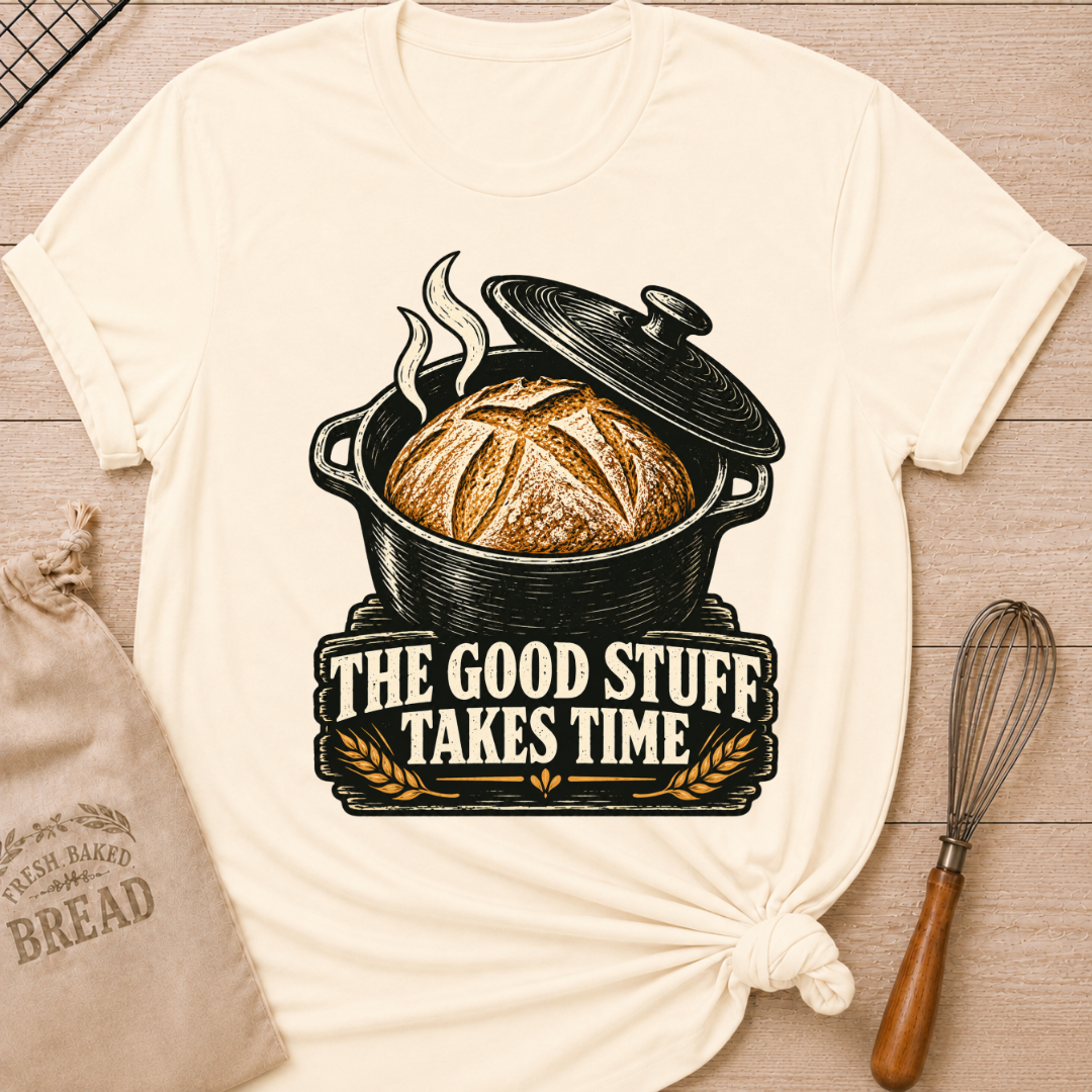 Natural women's relaxed fit tee with a golden artisan loaf rising from a vintage Dutch oven, steam curling overhead and wheat accents below, with The Good Stuff Takes Time lettering