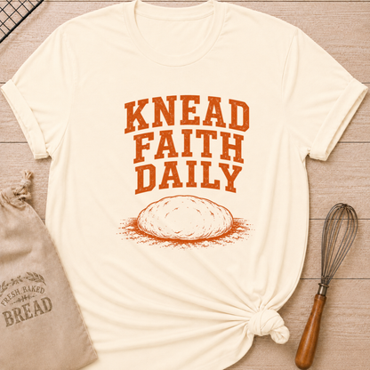 Natural women's relaxed fit t-shirt with the words Knead Faith Daily in strong vintage lettering with a simple hand-drawn loaf in a classic bake shop style.