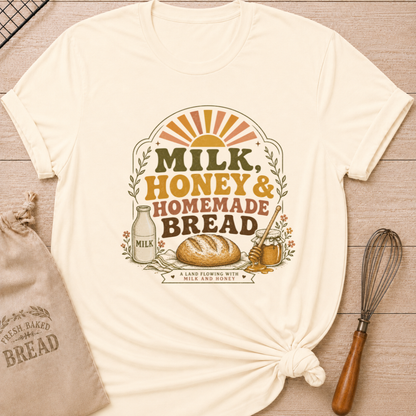 Natural women's relaxed fit t-shirt with the words Milk, Honey & Homemade Bread in vintage lettering with a rustic loaf, an old-fashioned milk bottle, and a jar of honey beneath a retro sunrise.