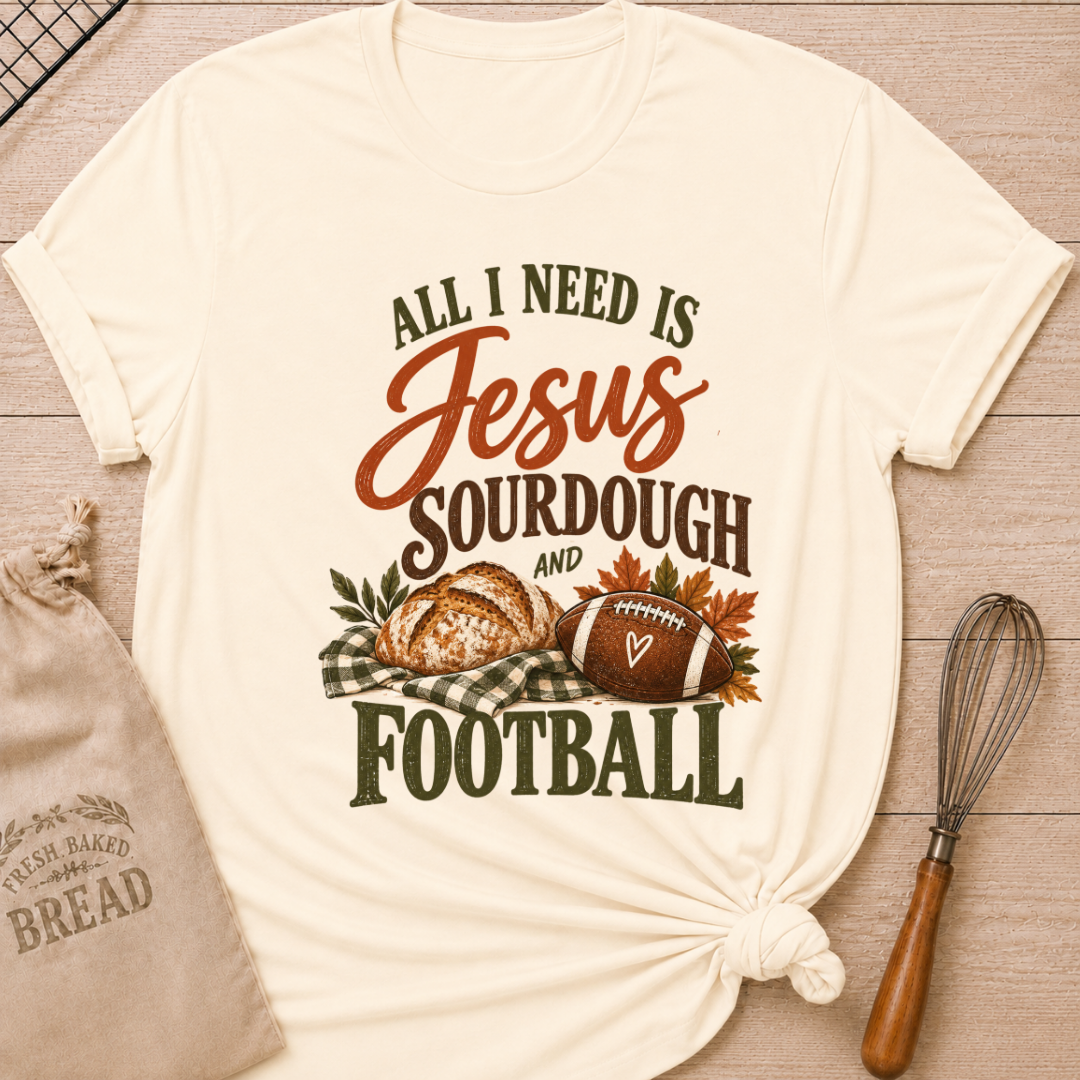Natural women's relaxed fit tee with bold vintage All I Need Is Jesus, Sourdough and Football lettering, a rustic sourdough loaf, classic football, gingham accents and autumn leaves in rich harvest tones