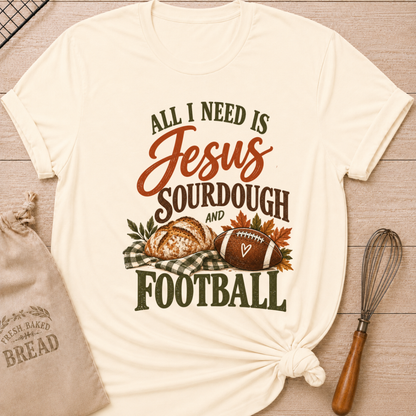 Natural women's relaxed fit tee with bold vintage All I Need Is Jesus, Sourdough and Football lettering, a rustic sourdough loaf, classic football, gingham accents and autumn leaves in rich harvest tones