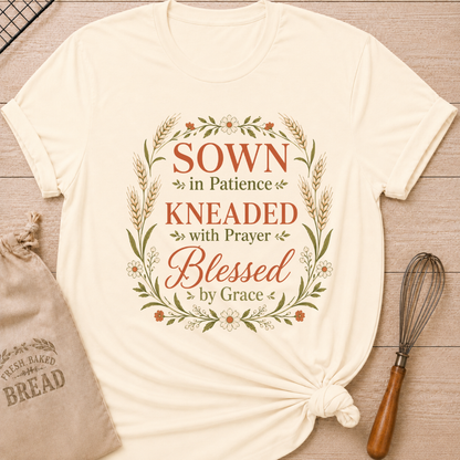 Natural women's relaxed fit t-shirt with the words Sown in Patience, Kneaded with Prayer, Blessed by Grace framed in wheat, daisies and delicate greenery.
