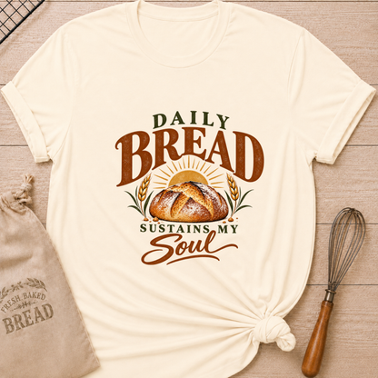 Natural women's relaxed fit tee with Daily Bread Sustains My Soul lettering around a golden artisan loaf beneath a rising sun, framed by wheat in rich earthy tones