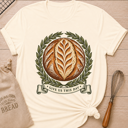 Natural women's relaxed fit tee with a scored artisan loaf framed by olive branches, finished with a vintage banner reading Give Us This Day