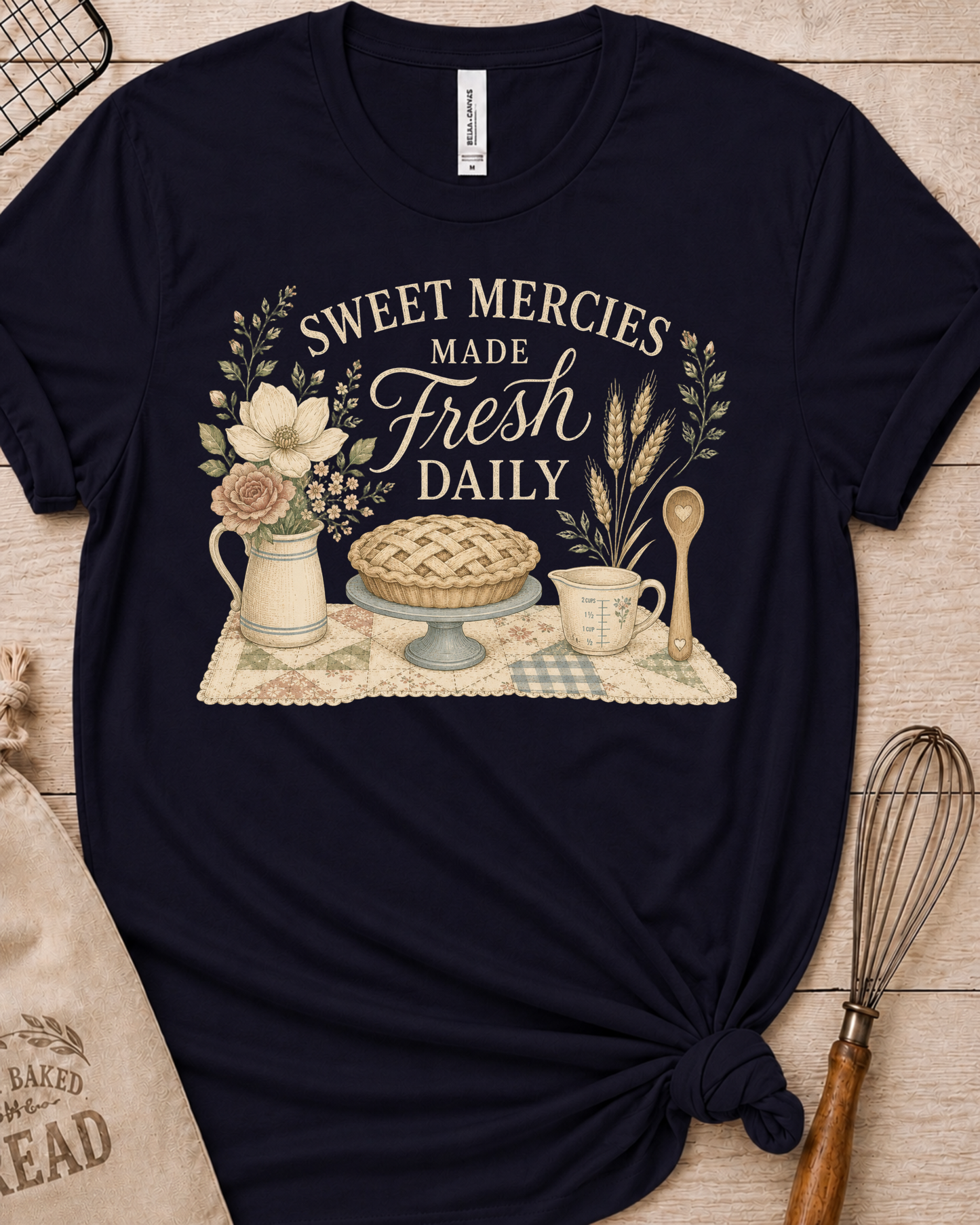Navy women's relaxed fit t-shirt reading Sweet Mercies Made Fresh Daily above a lattice-top pie on a cake stand with a flower pitcher, measuring cup, and wooden spoon.