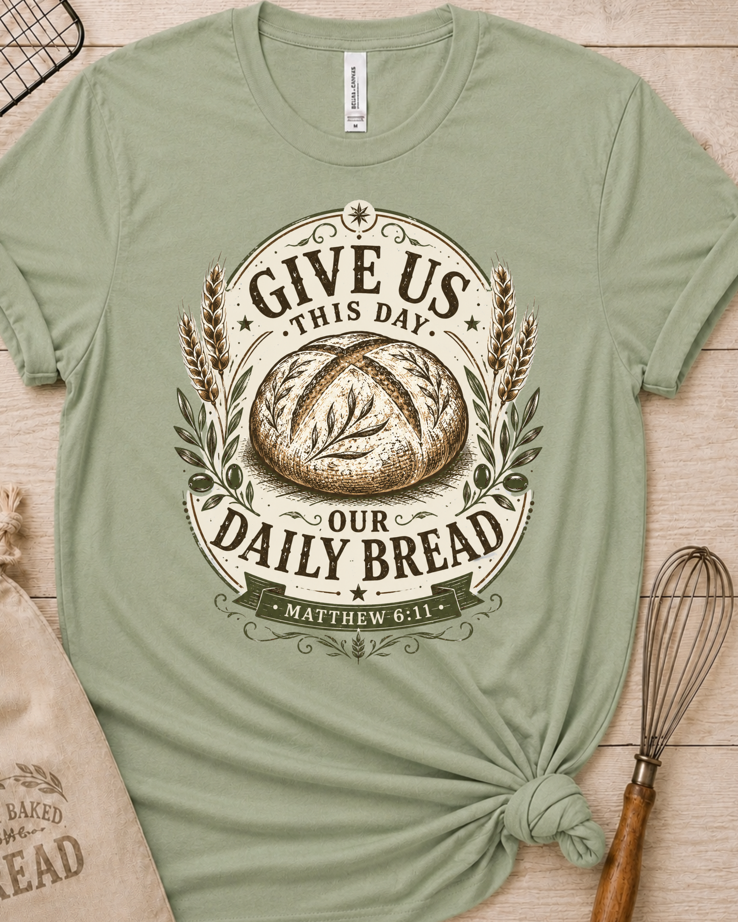 Sage green women's relaxed fit t-shirt with the Daily Bread emblem printed in cream, a clean badge-style bread illustration inspired by Matthew 6:11.