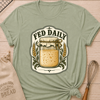 Sage women's relaxed fit tee with a bubbly sourdough starter jar framed by golden wheat and leafy accents in a vintage bakery label, with Fed Daily lettering