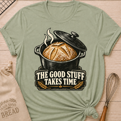 Sage women's relaxed fit tee with a golden artisan loaf rising from a vintage Dutch oven, steam curling overhead and wheat accents below, with The Good Stuff Takes Time lettering