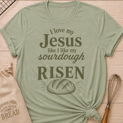 Sage green women's relaxed fit t-shirt with the words I Love My Jesus Like I Like My Sourdough, Risen in bold vintage lettering and a rustic loaf of bread.