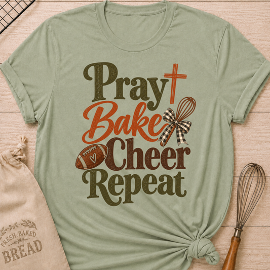 Sage women's relaxed fit tee with bold vintage Pray Bake Cheer Repeat lettering, a football, whisk, cross and gingham bow in warm autumn tones