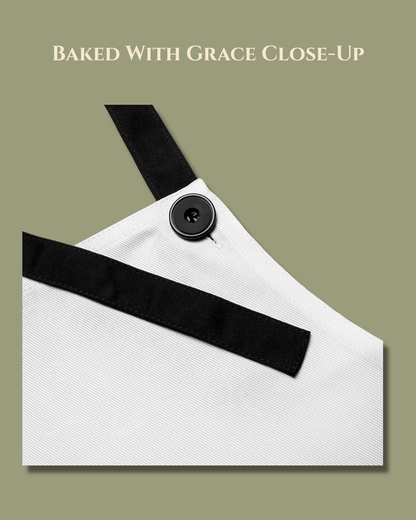 Close-up of the Baked with Grace apron in simple white, showing the black adjustable neck strap and button detail.