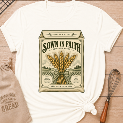 Vintage White women's relaxed fit tee with a vintage heirloom seed packet design, golden wheat, rolling fields and John 12:24 woven into the artwork beneath Sown in Faith lettering