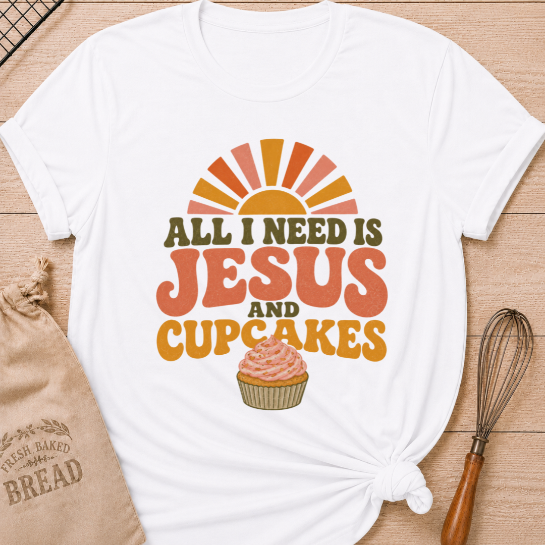 White All I Need Is Jesus and Cupcakes women's relaxed fit tee with retro lettering and a pink frosted cupcake in warm sunrise colors