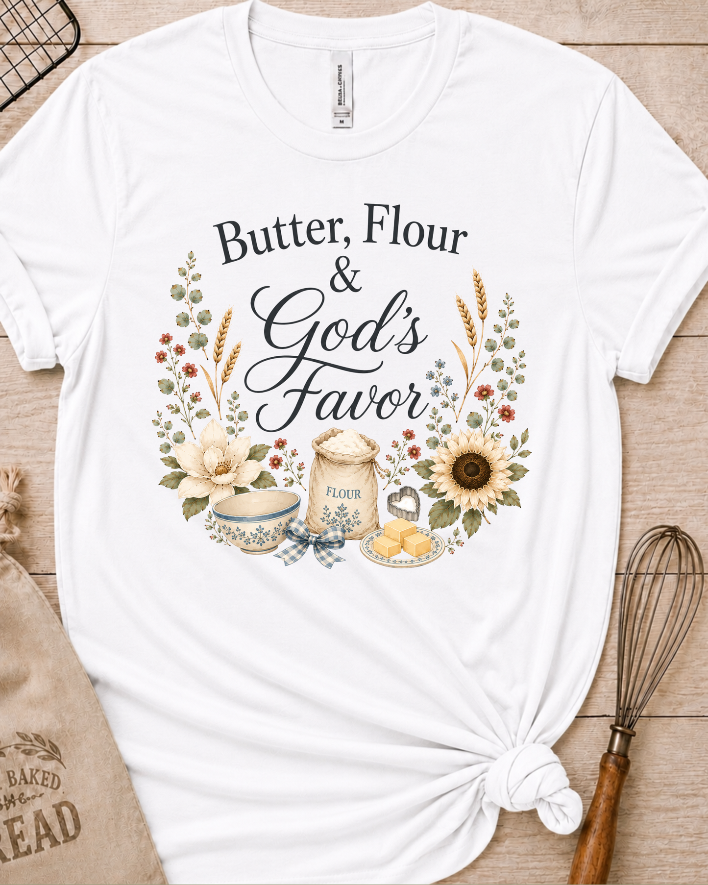 White women's relaxed fit t-shirt reading Butter, Flour and God's Favor, framed by a flour sack, a mixing bowl, butter, a sunflower, and wildflowers.