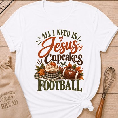 White women's relaxed fit tee with bold vintage All I Need Is Jesus, Cupcakes and Football lettering, a pumpkin topped cupcake, autumn leaves and a football on a gingham blanket