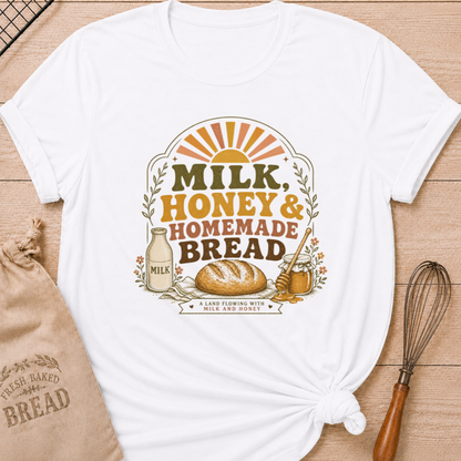 White women's relaxed fit t-shirt with the words Milk, Honey & Homemade Bread in vintage lettering with a rustic loaf, an old-fashioned milk bottle, and a jar of honey beneath a retro sunrise.