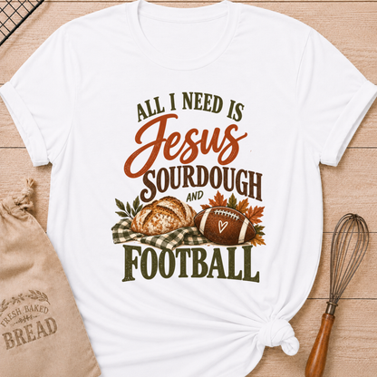 White women's relaxed fit tee with bold vintage All I Need Is Jesus, Sourdough and Football lettering, a rustic sourdough loaf, classic football, gingham accents and autumn leaves in rich harvest tones